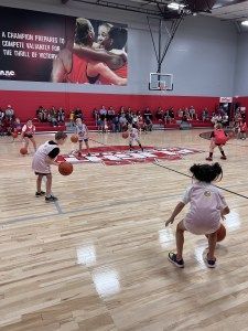 Youth basketball game in a gymnasium. Children dribble the ball. Spectators watch from the sidelines.