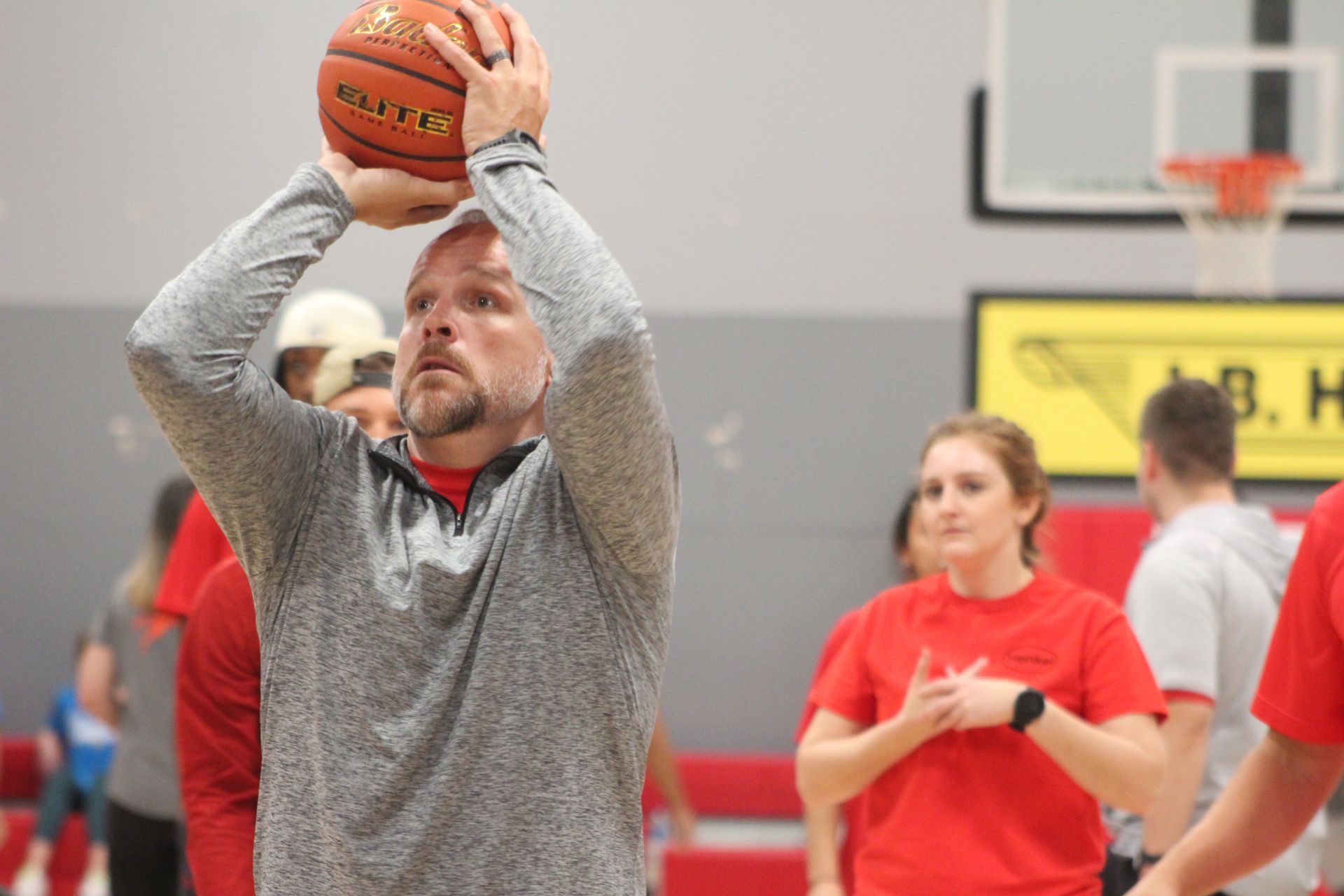 Man with dreadlocks holding a basketball, in a gym, looking up. Wearing a black shirt and blue pants.