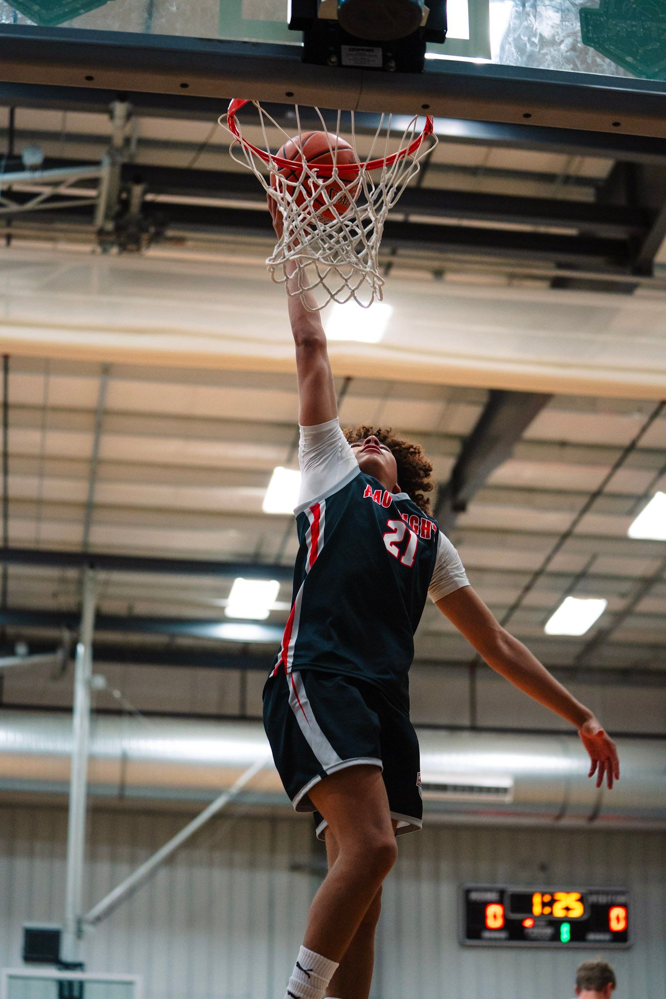 Basketball player dunking the ball. He is wearing a black jersey with white trim. Game is in progress.