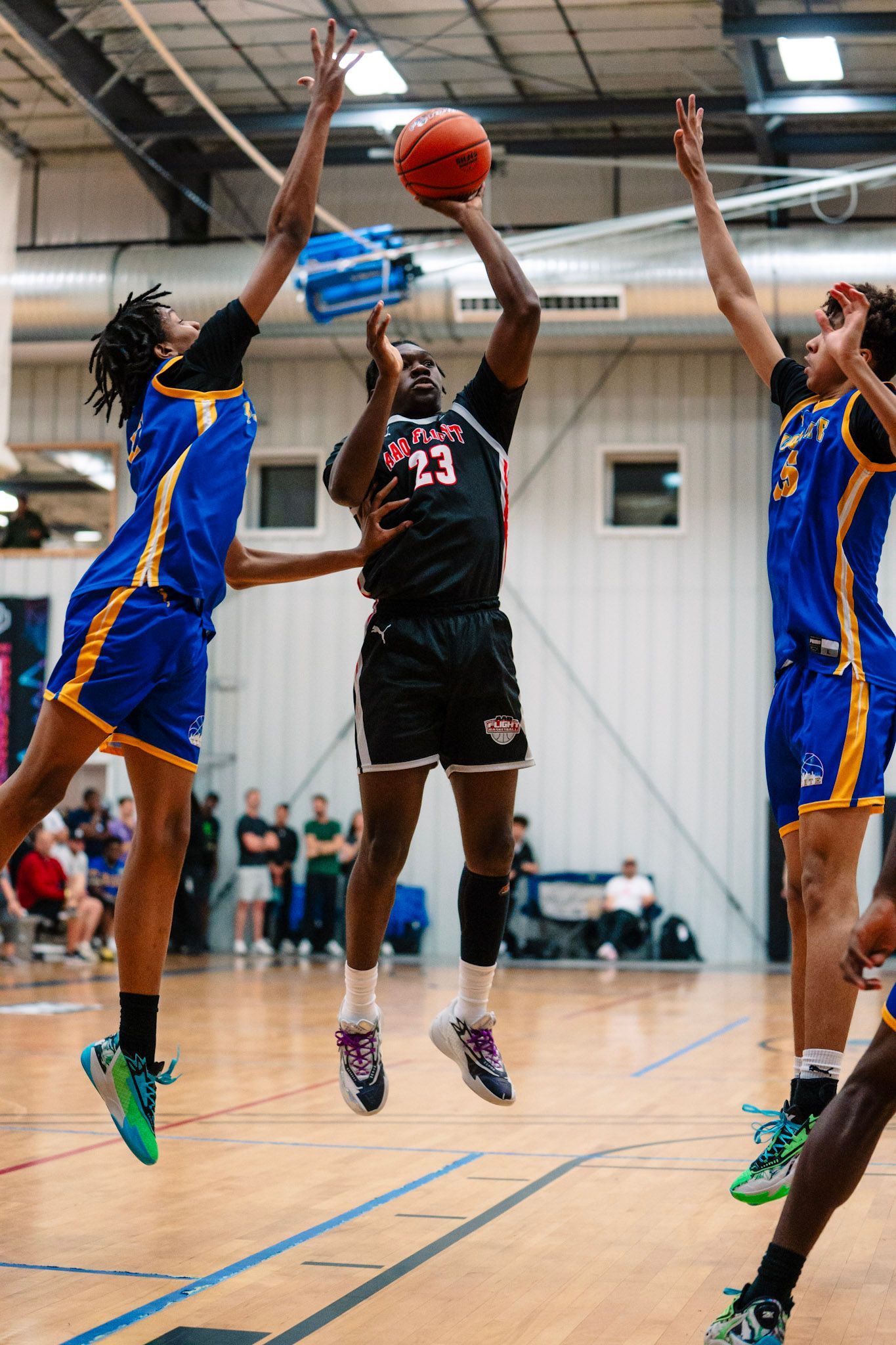 Basketball player shooting over defenders in a gym.