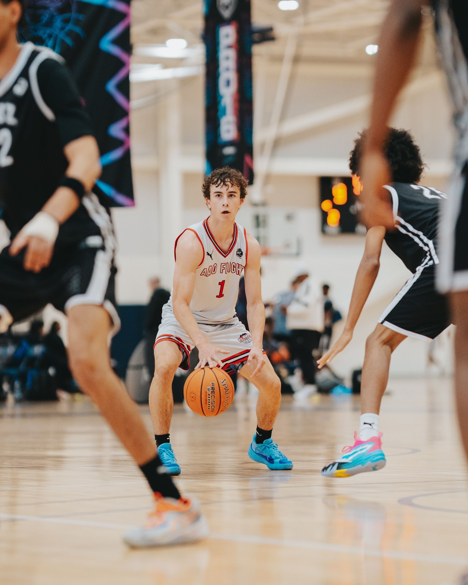 Basketball player dribbling the ball, focused, on a court with two opposing players.