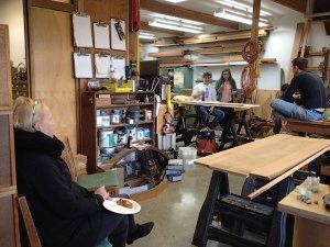 A woman is sitting in a chair in a workshop holding a plate of food.