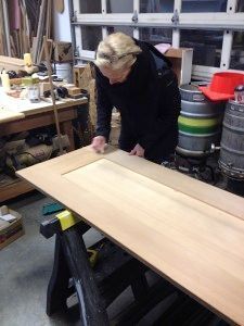 A woman is working on a wooden door in a workshop.