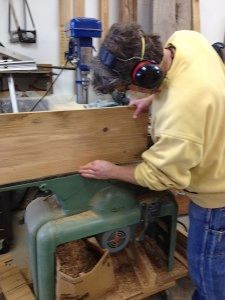 A man wearing headphones is cutting a piece of wood on a machine.