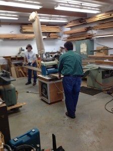 A man in a green shirt is standing in a woodworking shop.