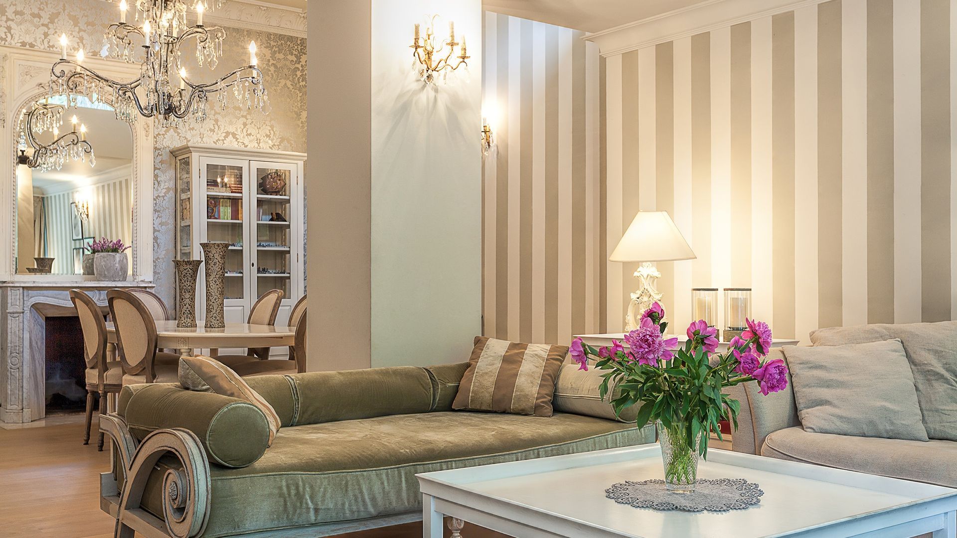 A living room with a striped wall , a couch , a table and a vase of flowers.