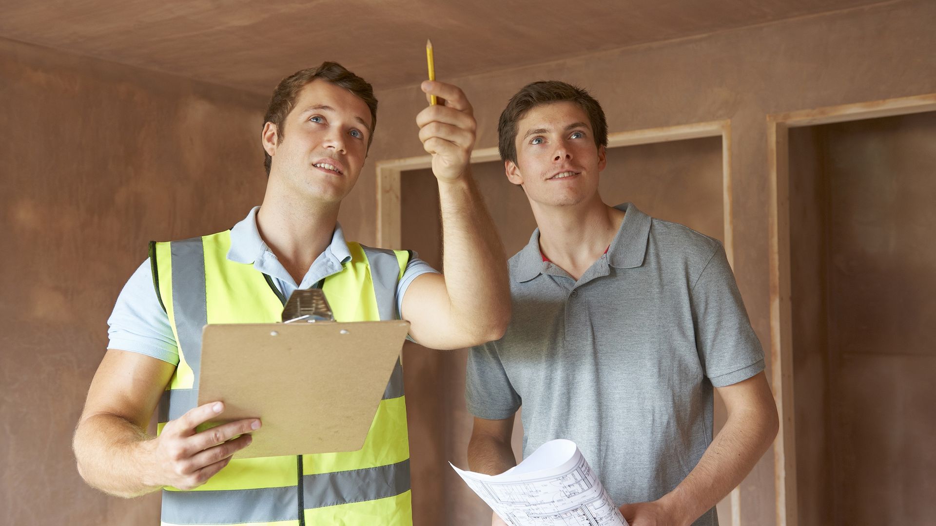 Two men are standing next to each other in a room looking at a clipboard.