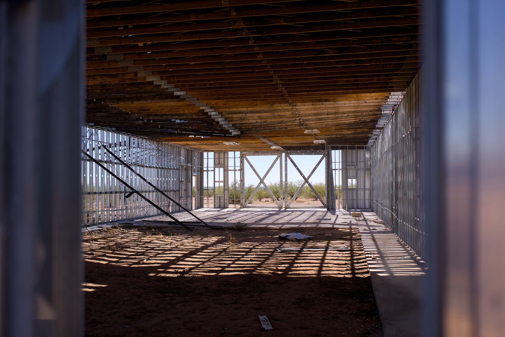 Interior of a construction site with metal framing, a low ceiling, and sunlight casting shadows on the floor.