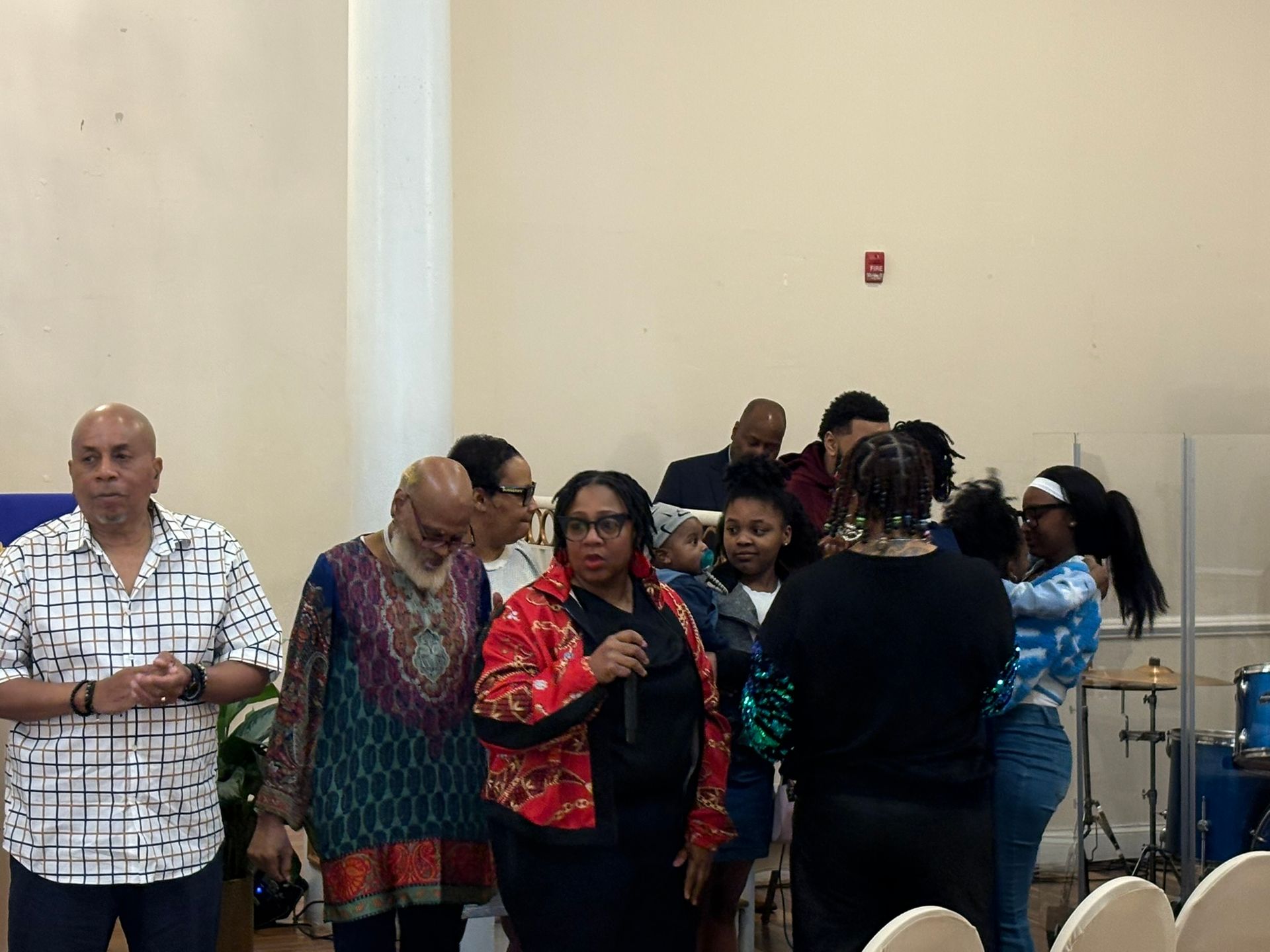 People standing and speaking at a church gathering, with microphones and a music stand in the background