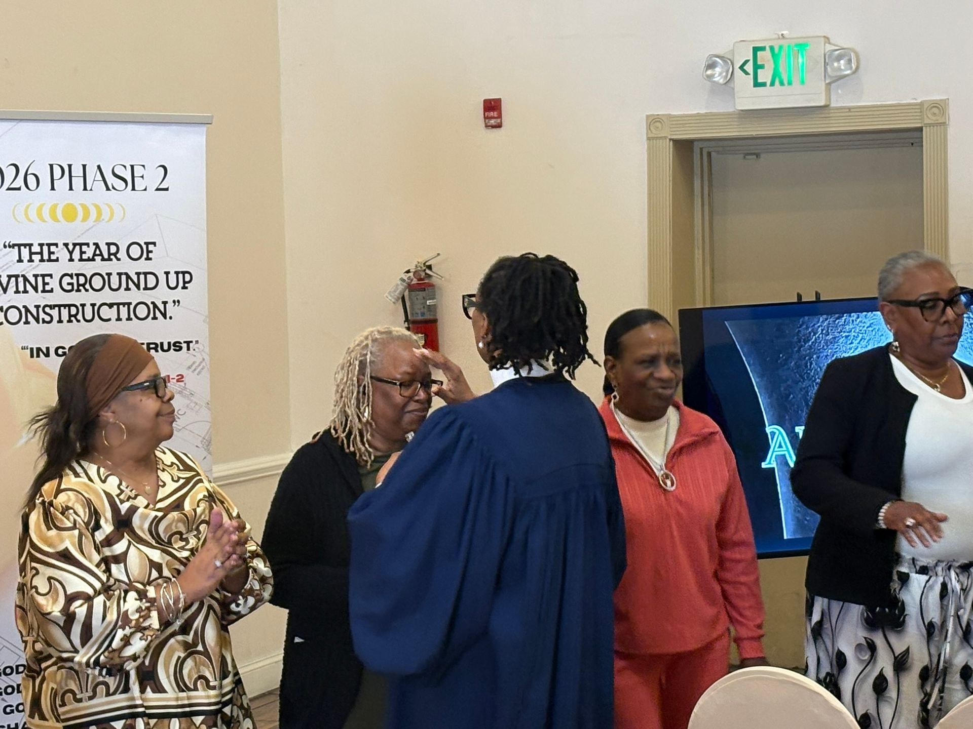 Five people standing and talking in a hallway near an exit sign and a construction notice.