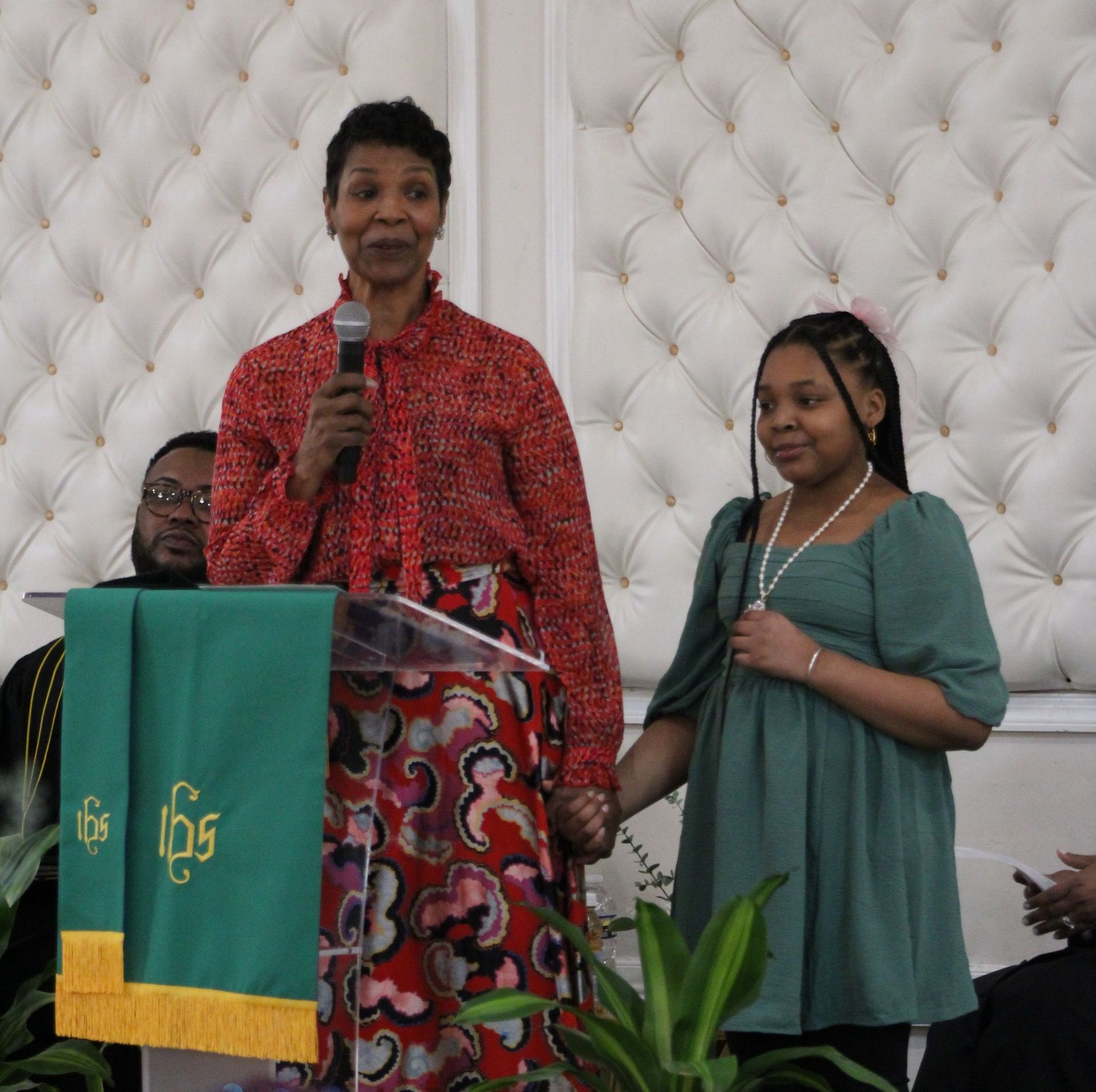 A woman stands at a podium with a green cloth that says 165 on it