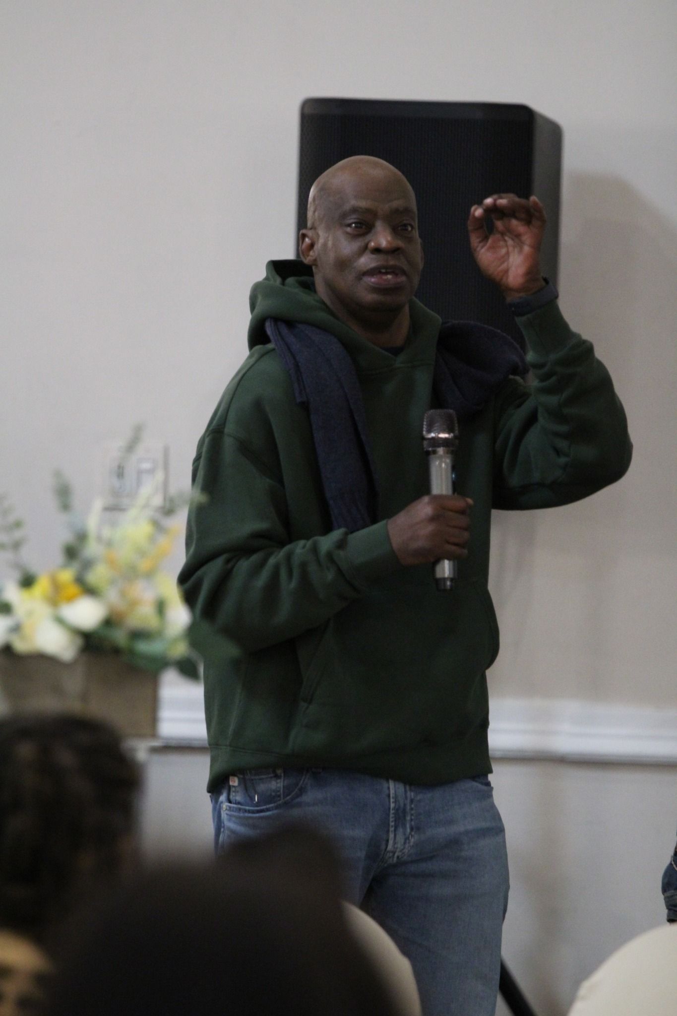 A man in a green hoodie is holding a microphone