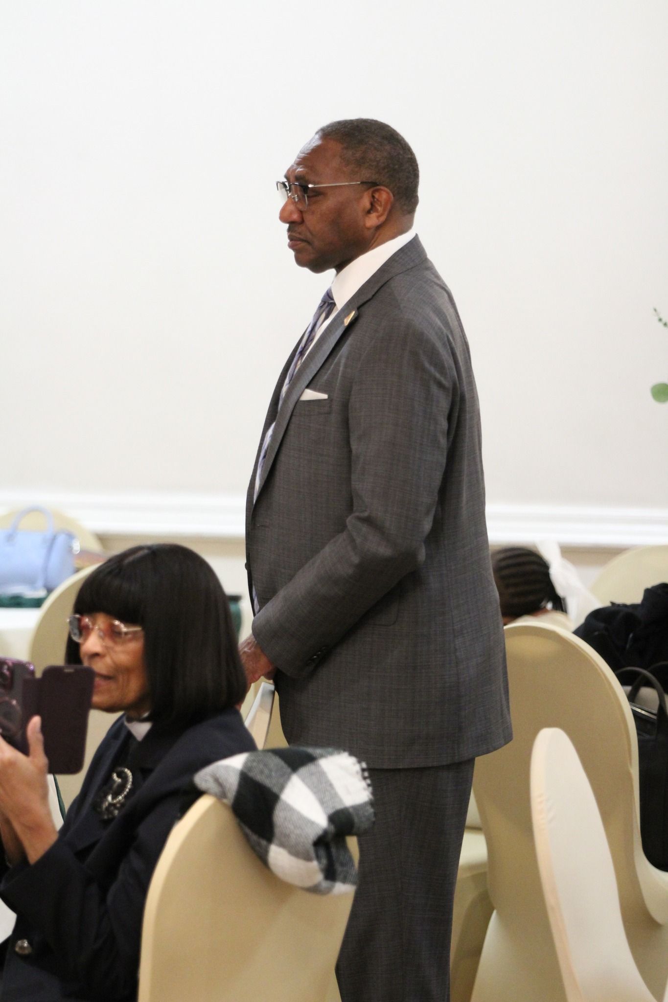 A man in a suit and tie is standing next to a woman in a chair