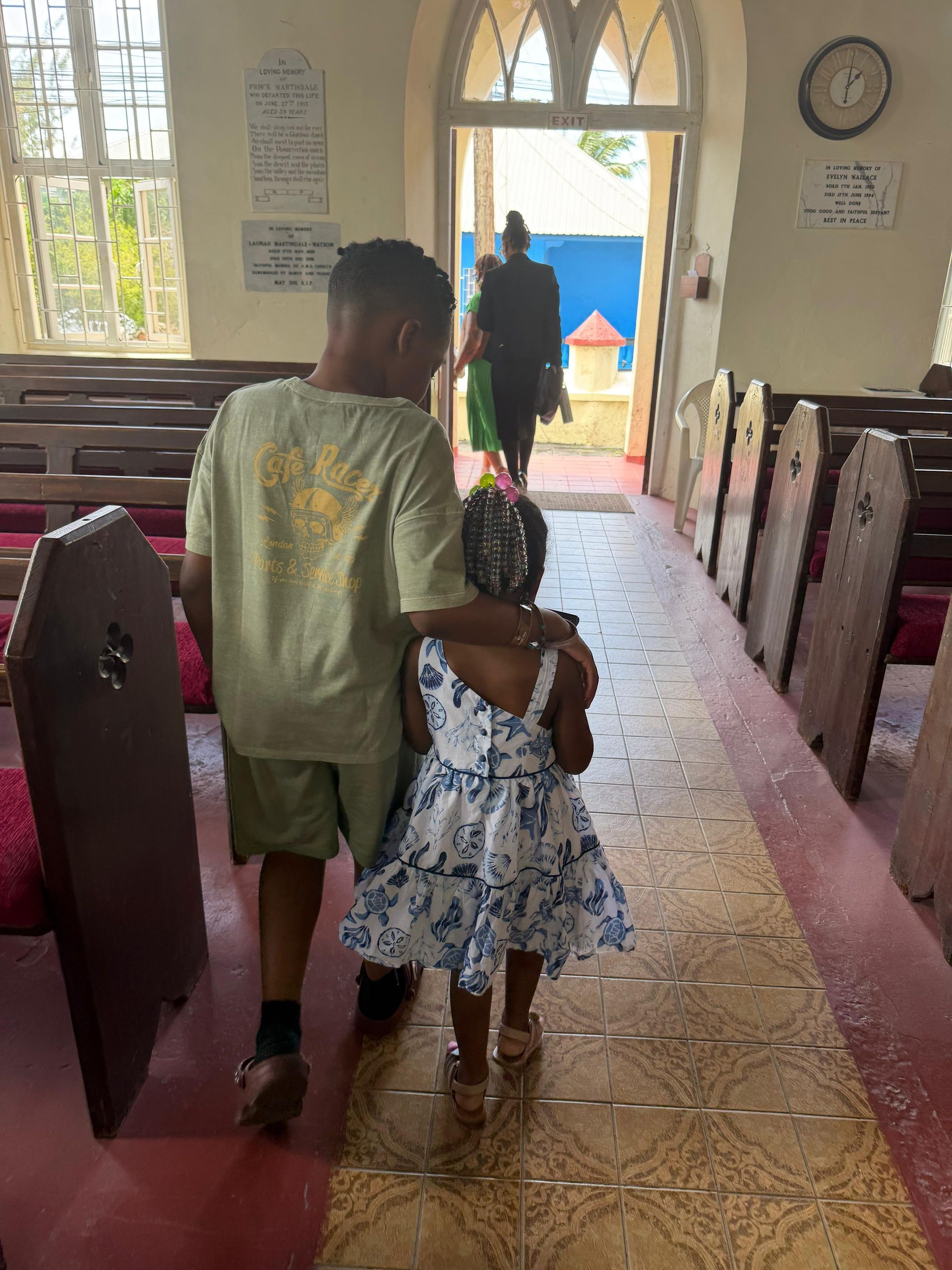 Two children walk down a church aisle toward the open doorway.