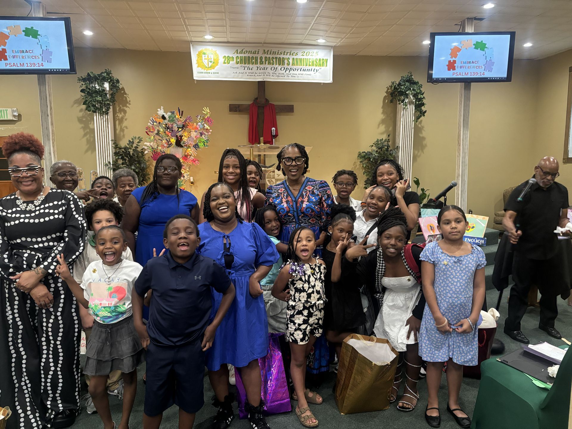 Group posing in a decorated church sanctuary, smiling in front of a pulpit with floral arrangements.