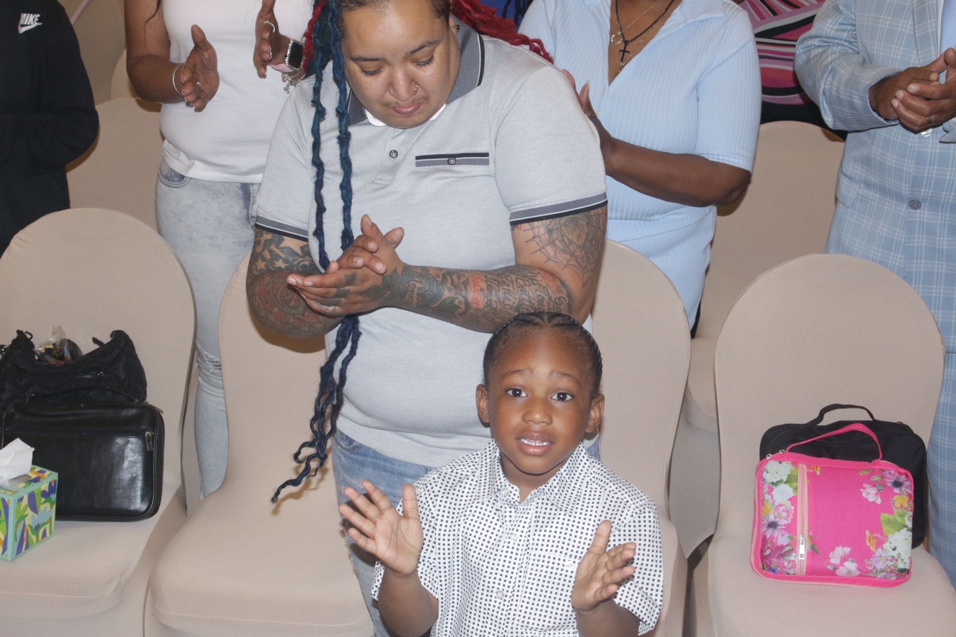 A child claps in front of seated adults at an indoor gathering.