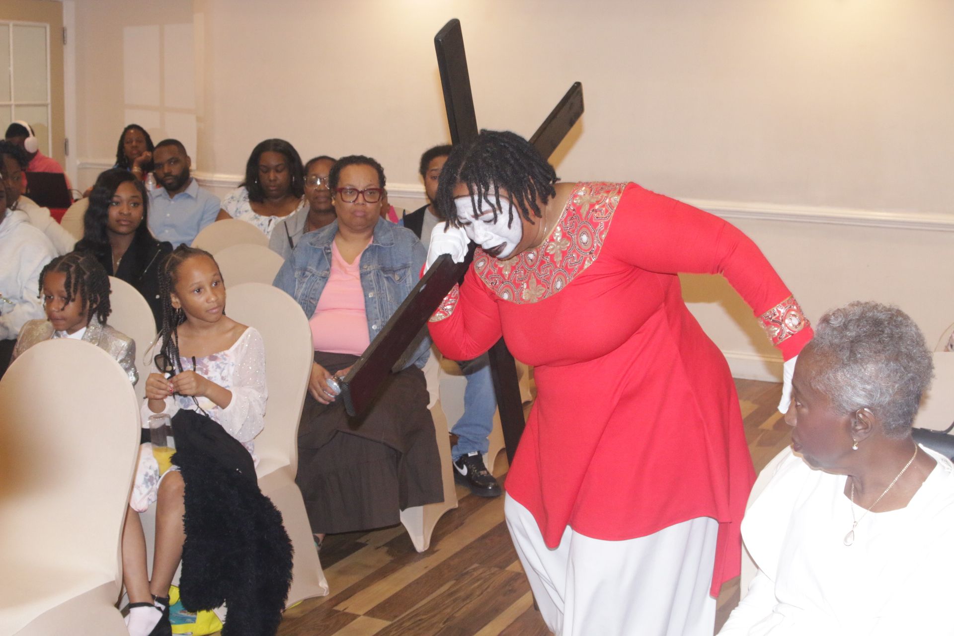 Woman in a red dress steps down an aisle in a church, with seated people watching nearby.