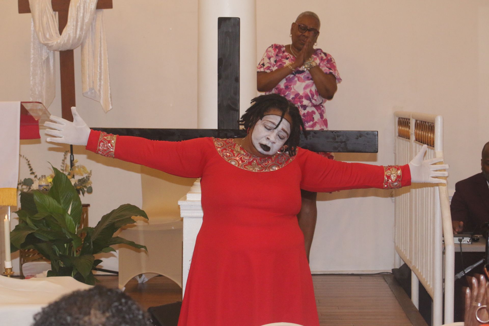 Person in red dress with arms outstretched in front of a cross inside a church sanctuary