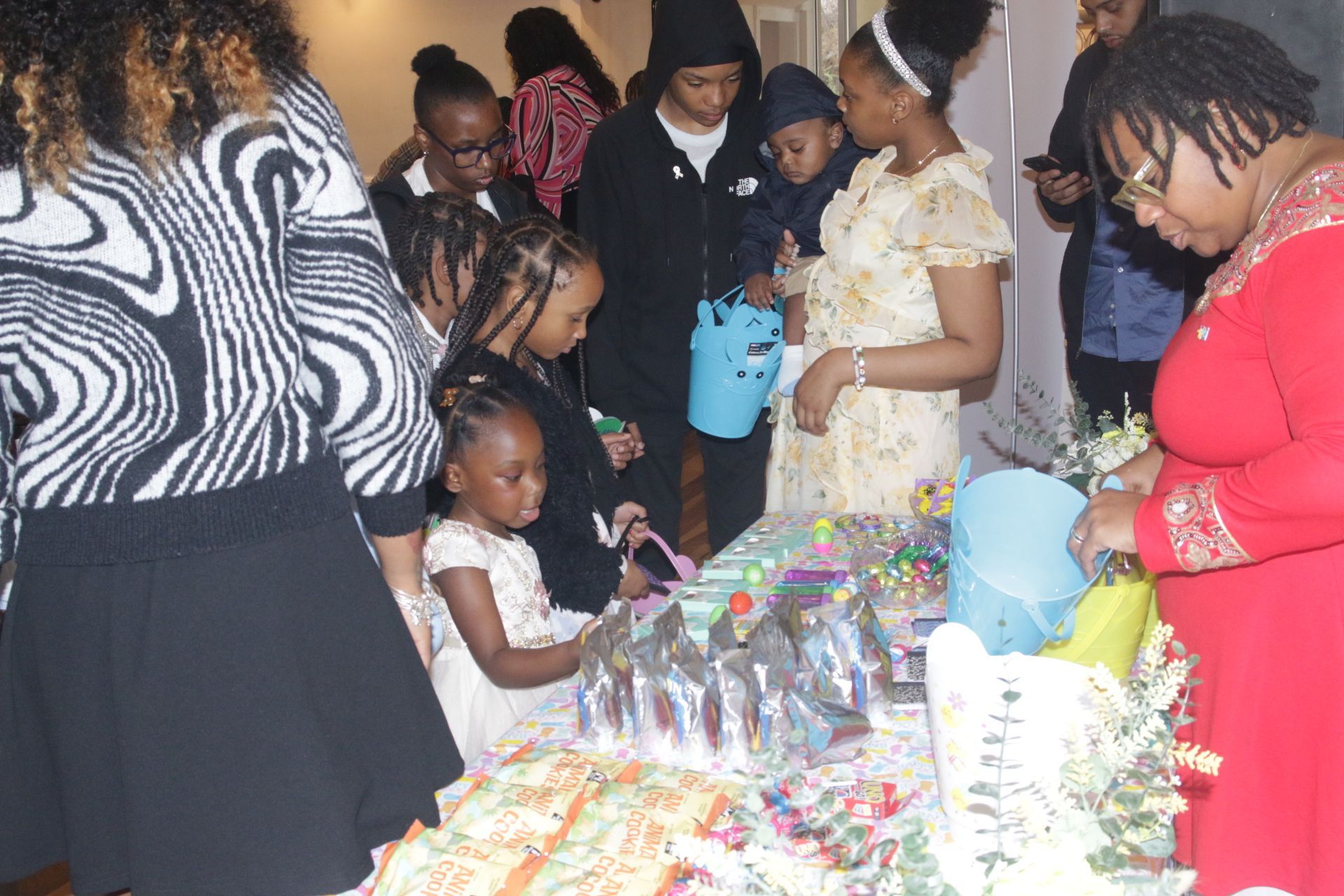 People gathered around a colorful gift table at a party, examining items and chatting.