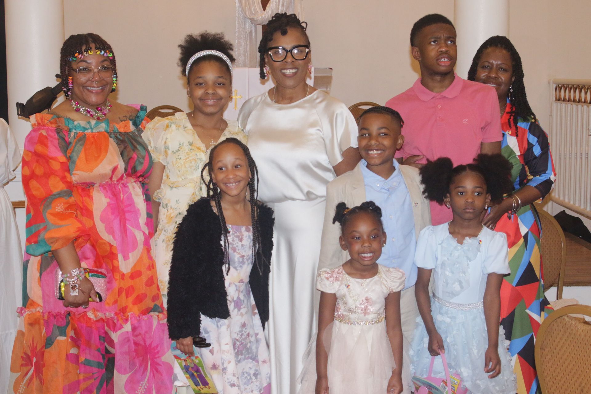 Eight people posed indoors for a family photo, dressed in colorful and formal clothes.