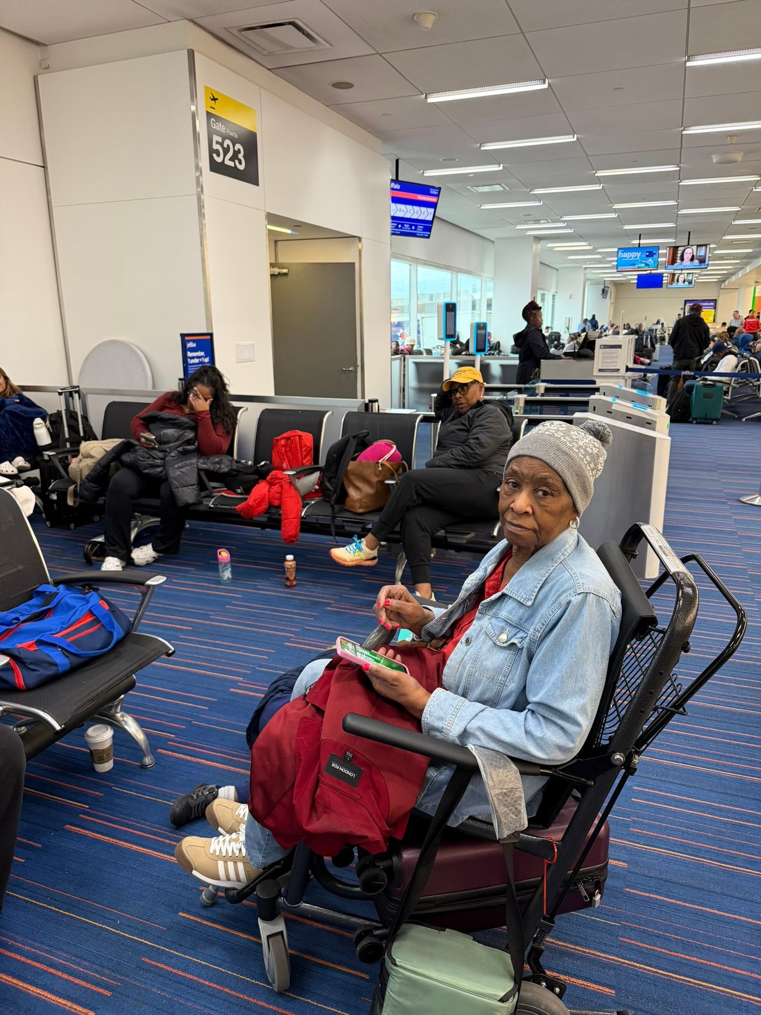 People waiting in an airport terminal, seated near luggage and a gate area.