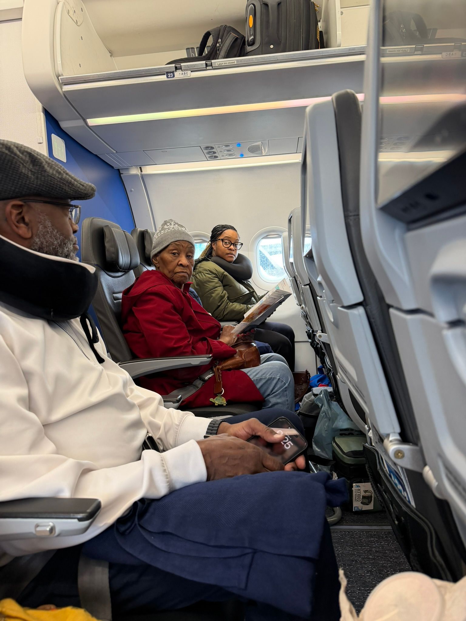 Passengers seated in an airplane cabin, some wearing coats and looking toward the camera