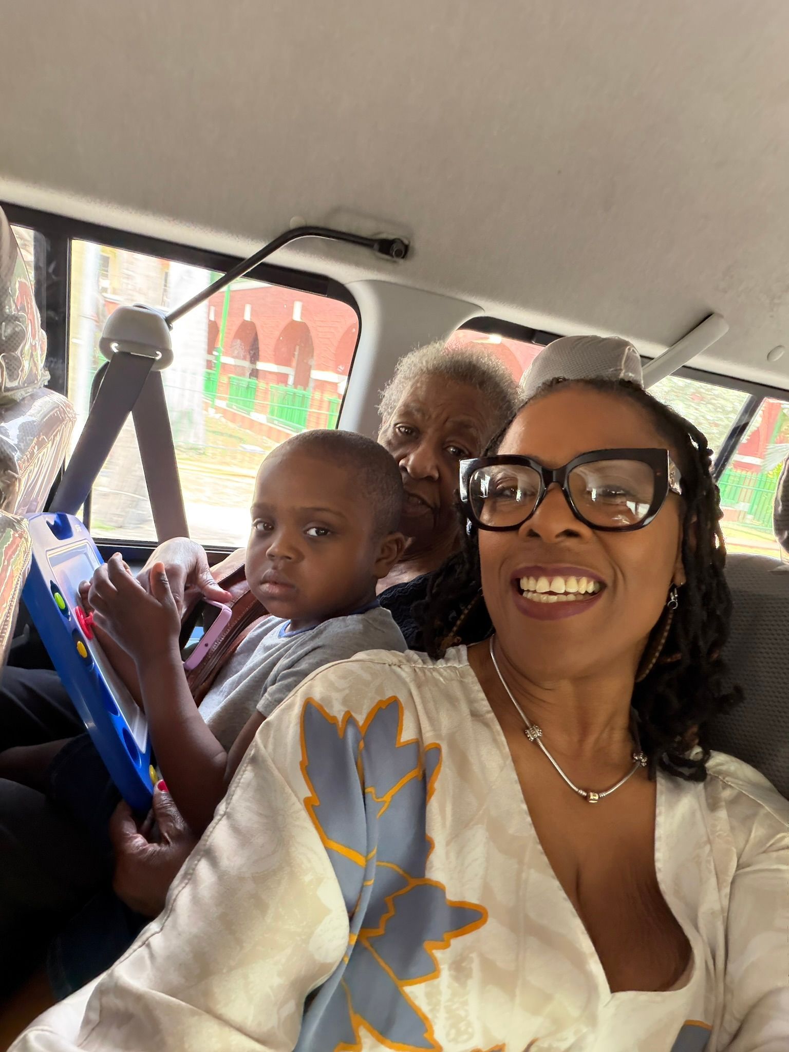 Three people smiling in a car, with a child holding a colorful tablet near the window.
