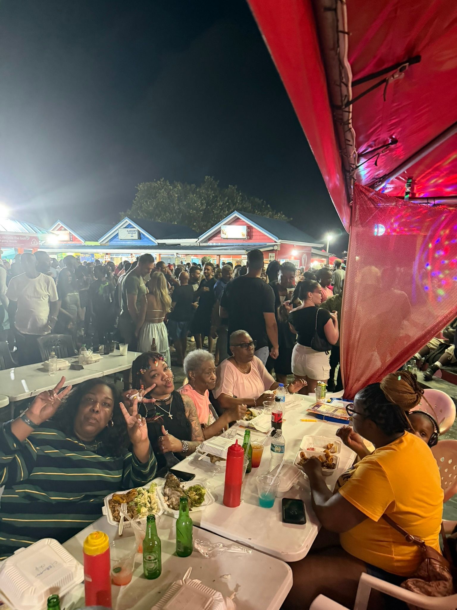People dining at a crowded outdoor night market with bright lights and red canopy decorations