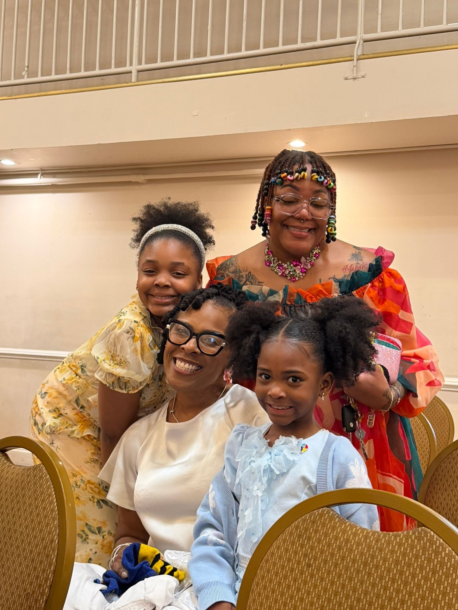 Four people smiling at a table, dressed in colorful outfits at an indoor event.