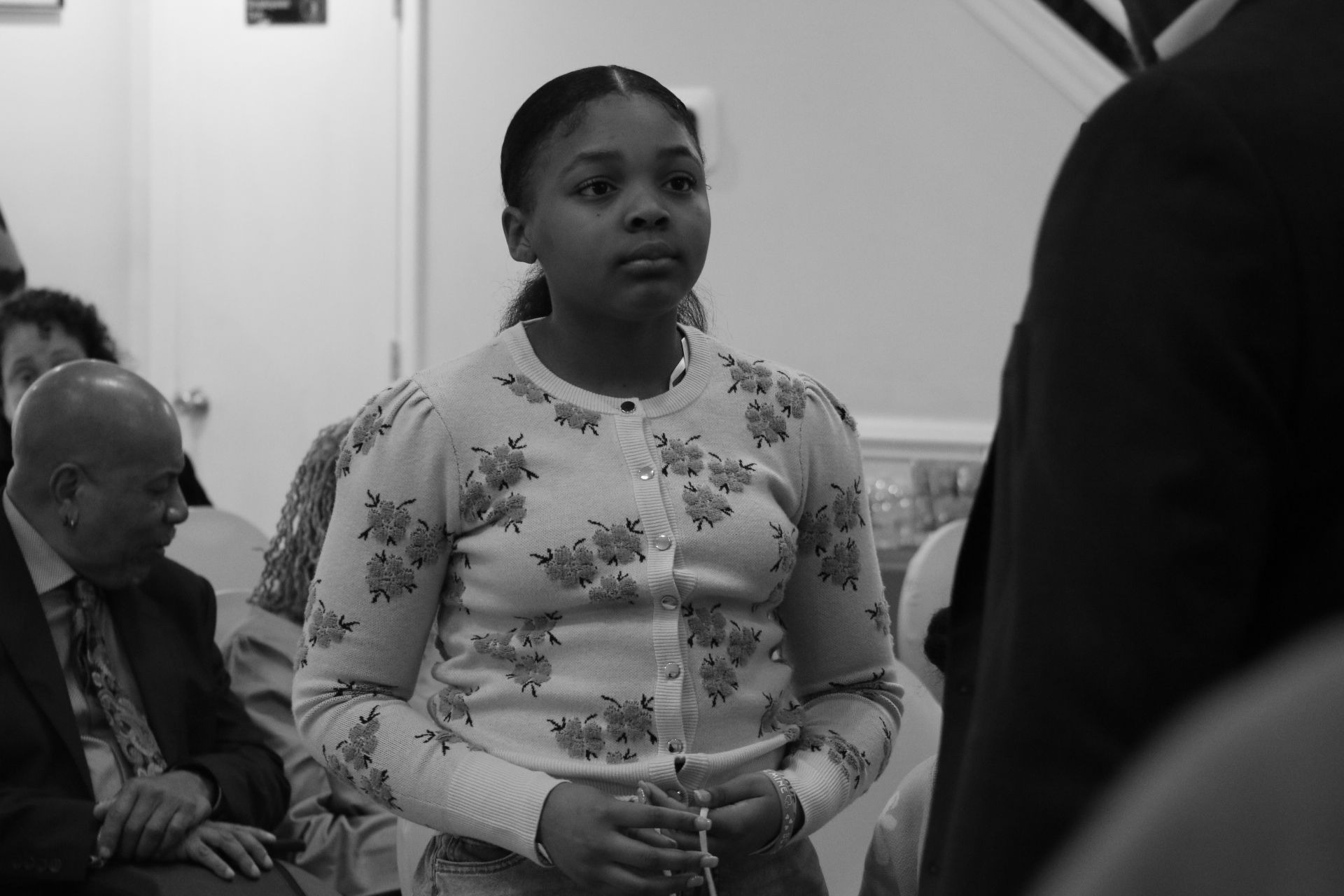 Woman standing indoors at a formal event, holding a cup and facing someone off-camera.