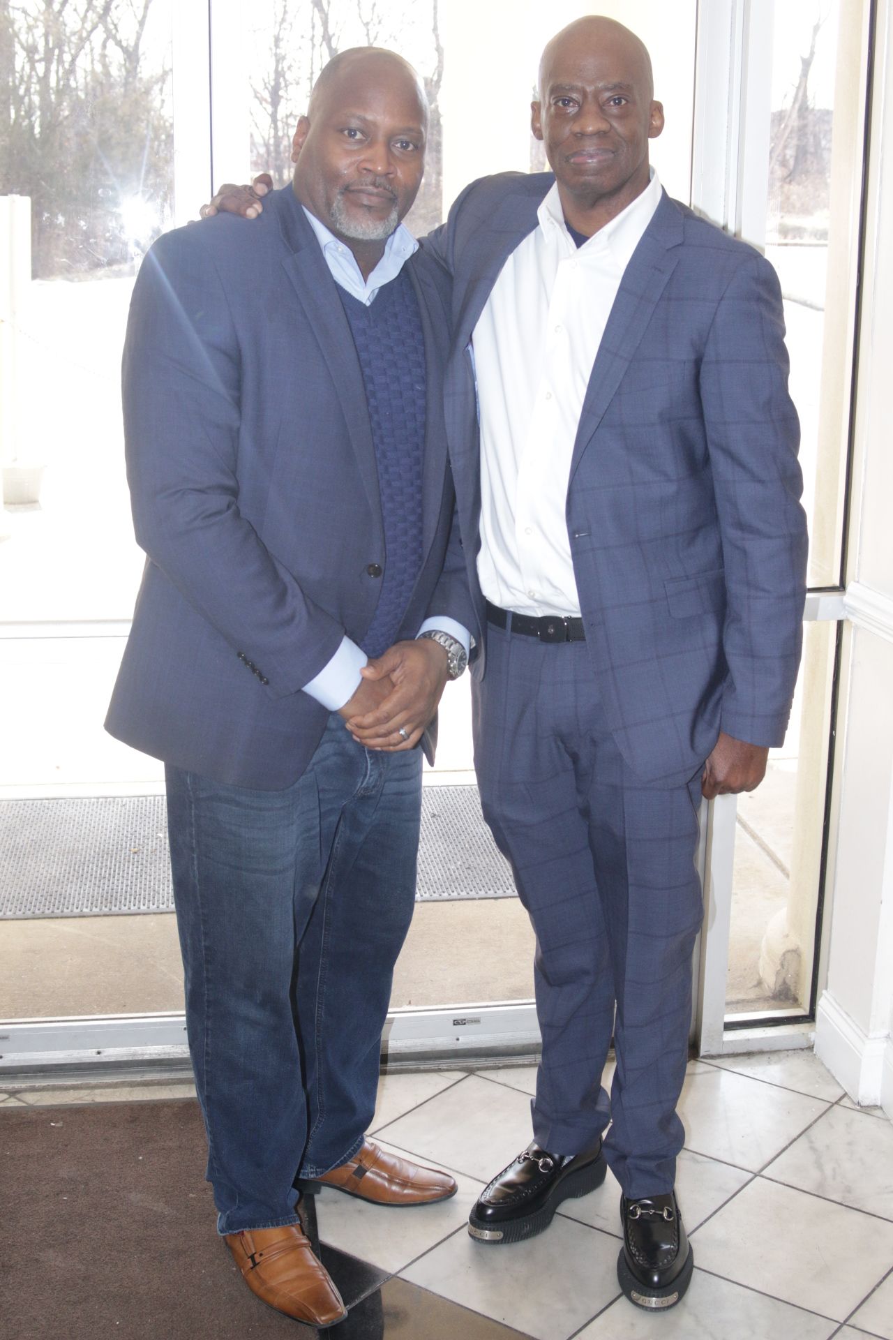 Two men in suits shaking hands indoors by a glass door