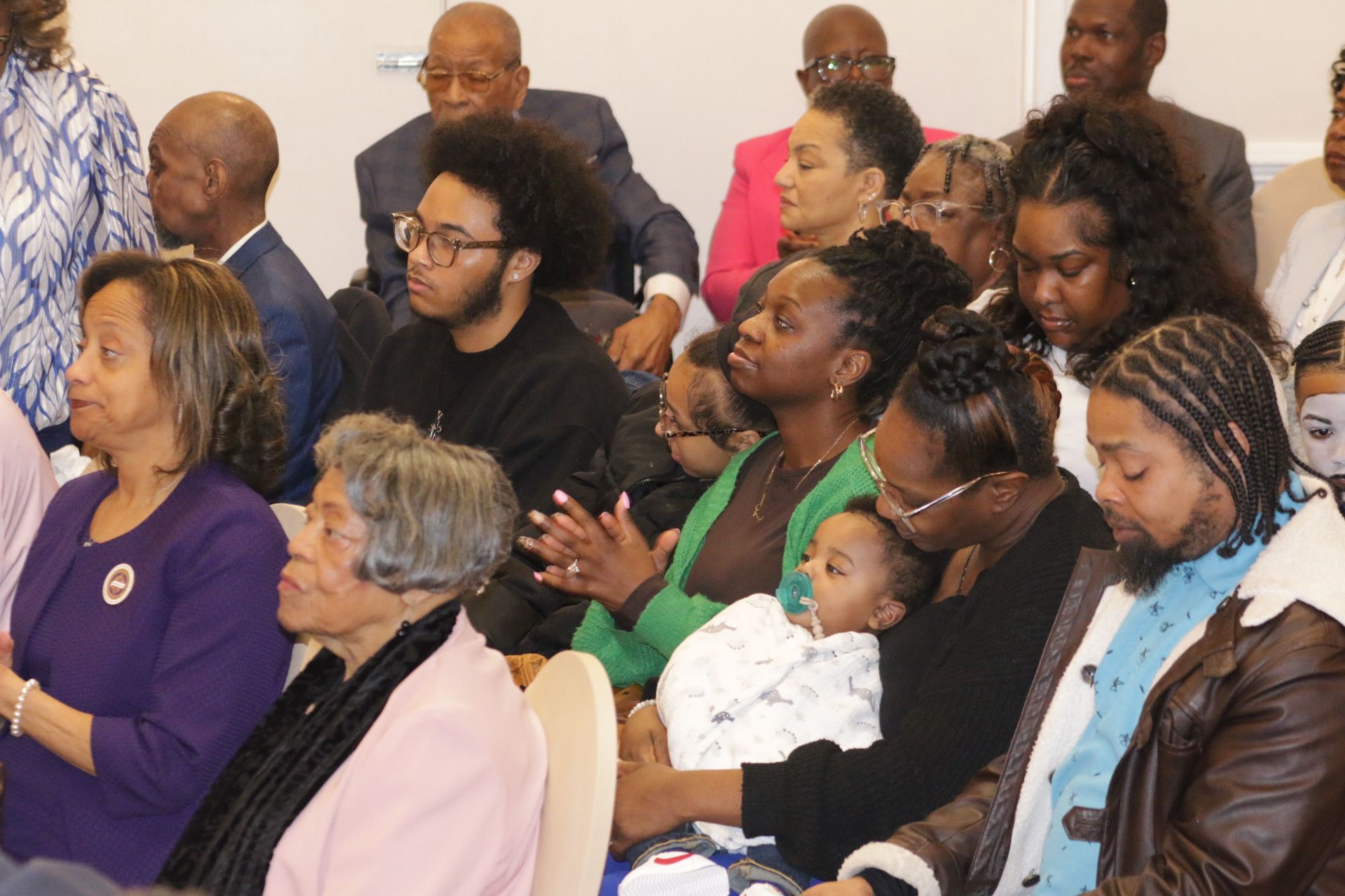 Audience seated in a room, listening attentively at a formal gathering.