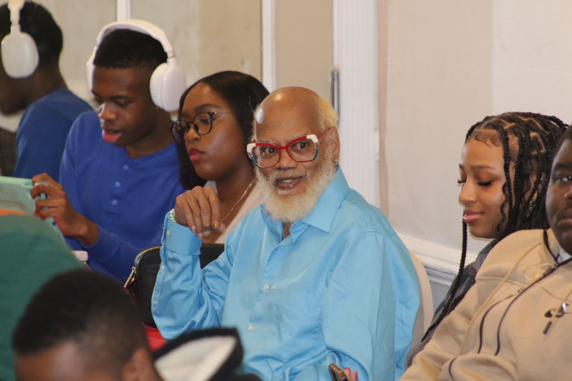 People seated in a meeting, with one man in a blue shirt listening attentively.