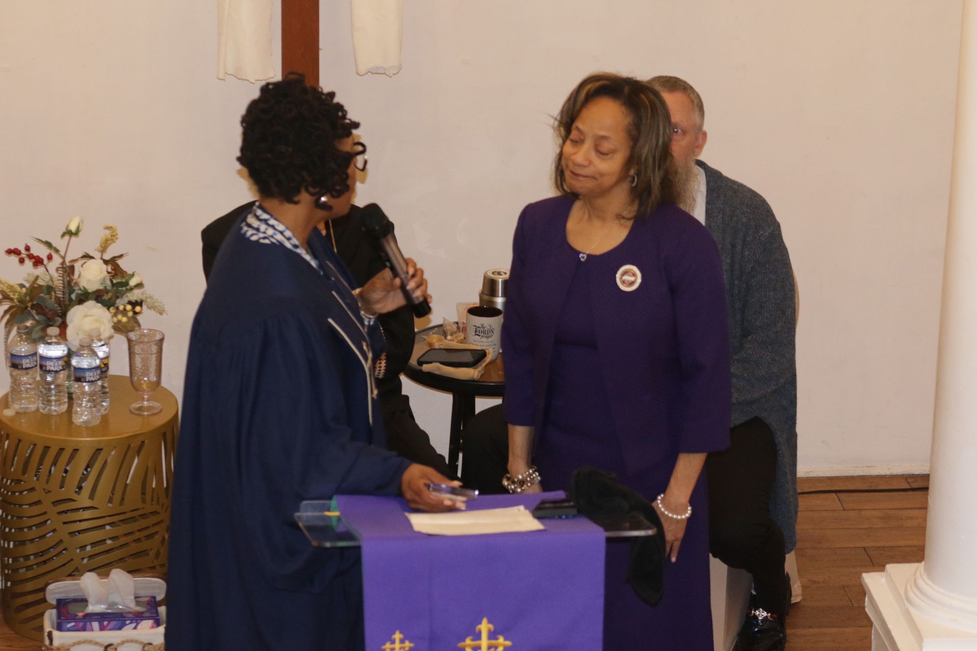Two women speaking at a purple-draped table during a formal indoor event