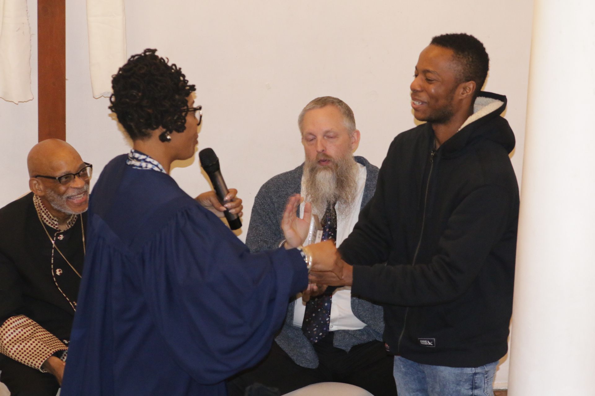 Three people exchanging a handshake and a certificate at an indoor event