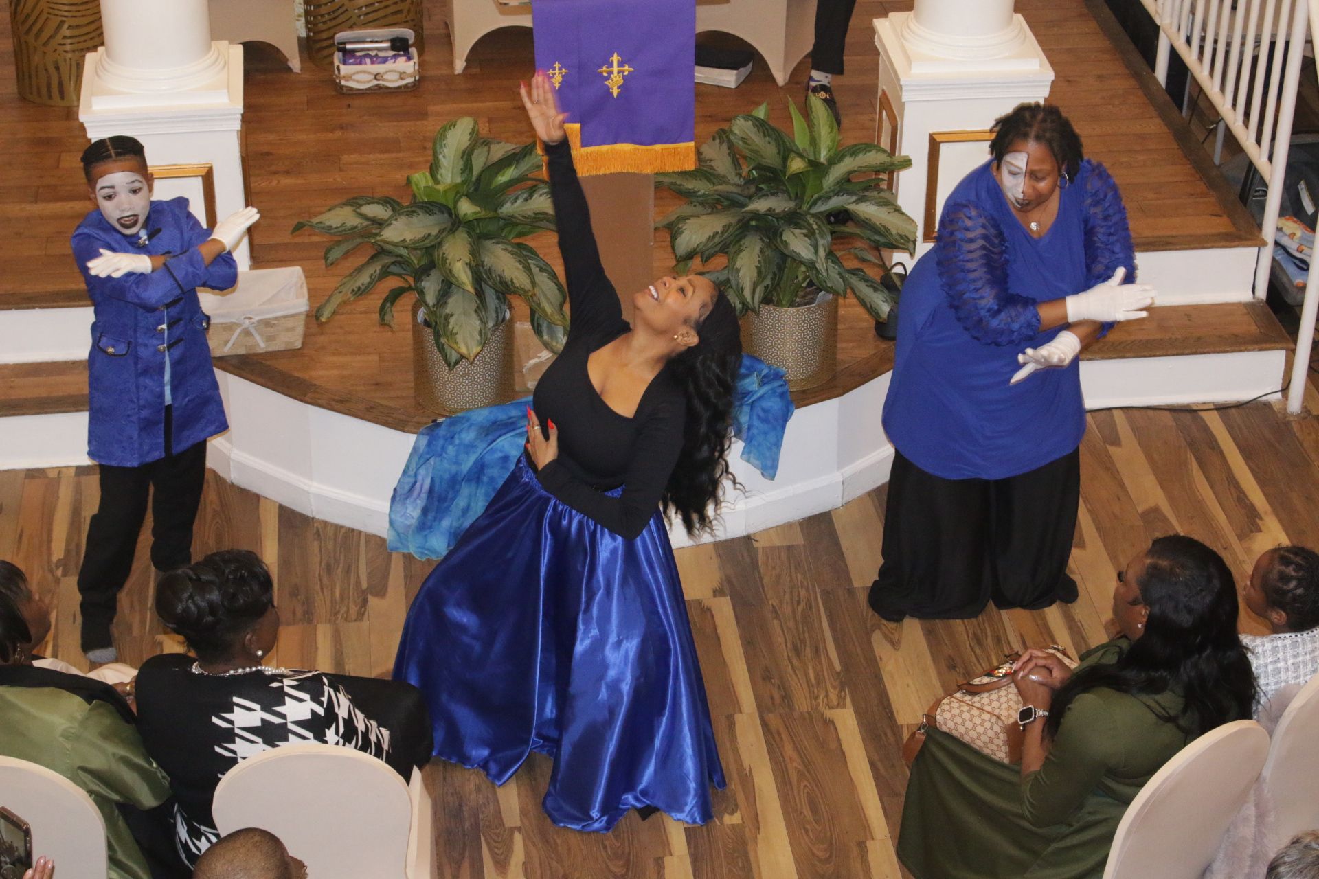 People performing a dance in a church sanctuary, with blue and black costumes and seated audience members nearby