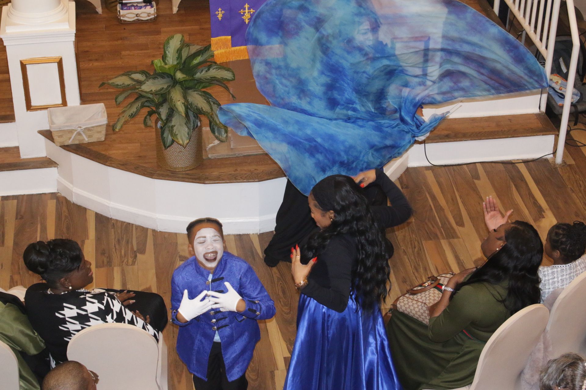 People in blue and black costumes performing on a church stage with a large blue backdrop