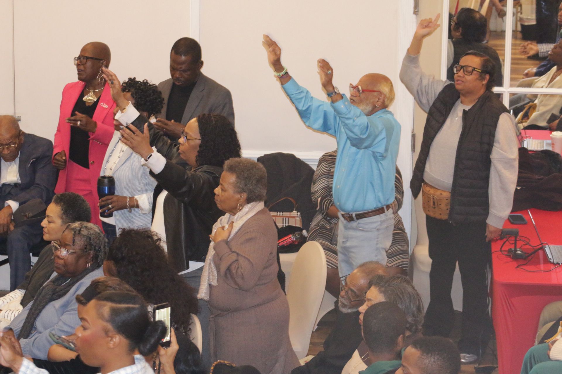 Audience standing and applauding at a lively indoor event, with one person raising both hands.