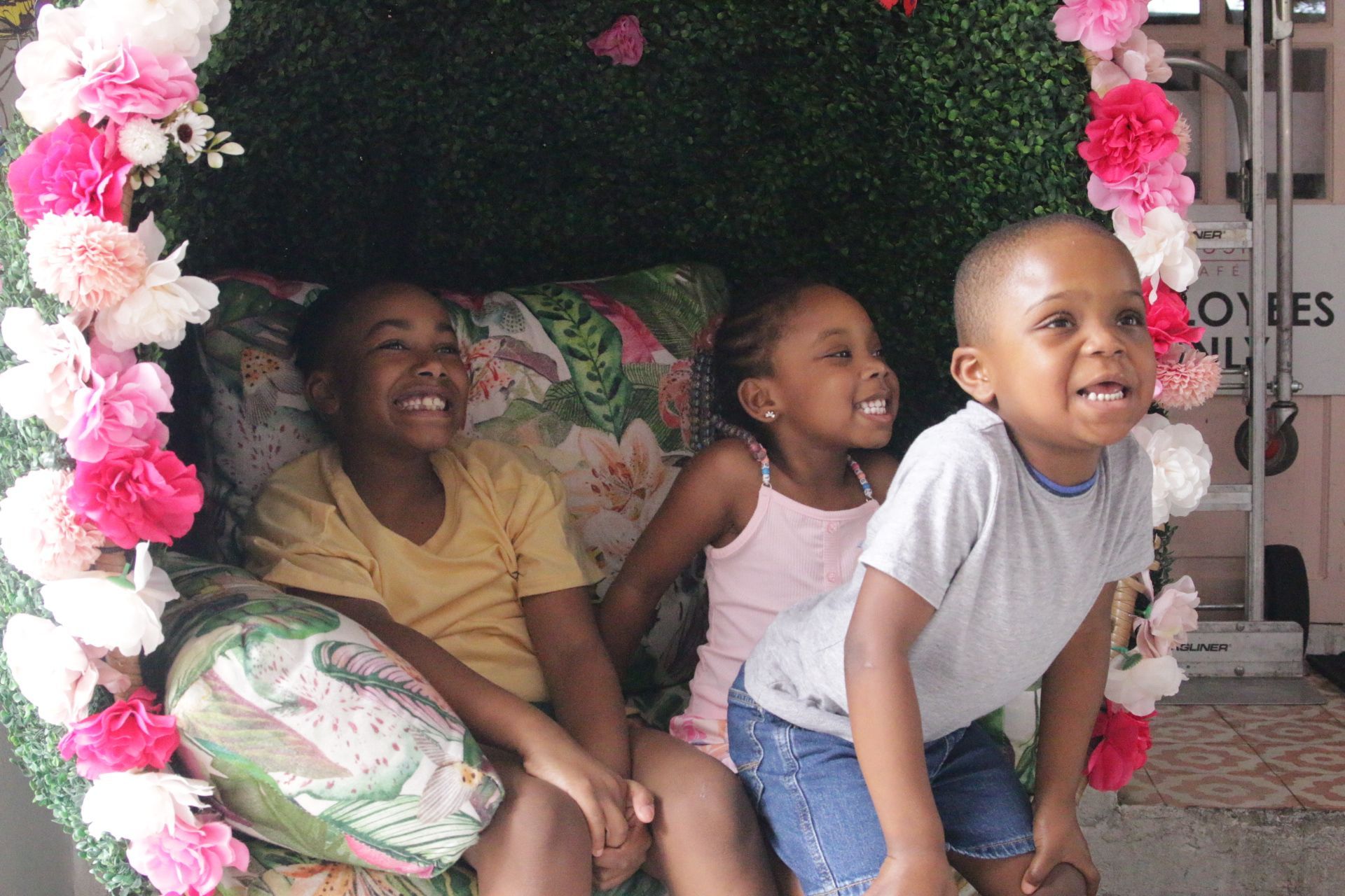 Three smiling children inside a pink and floral play nook, one leaning forward in the foreground.