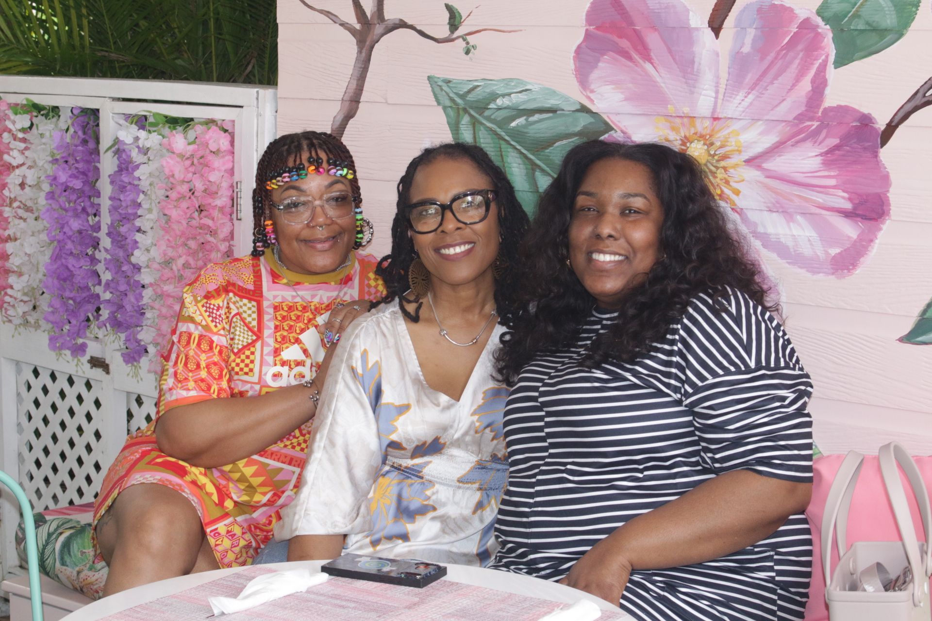 Three people smiling on a couch in front of floral wall decor at a table