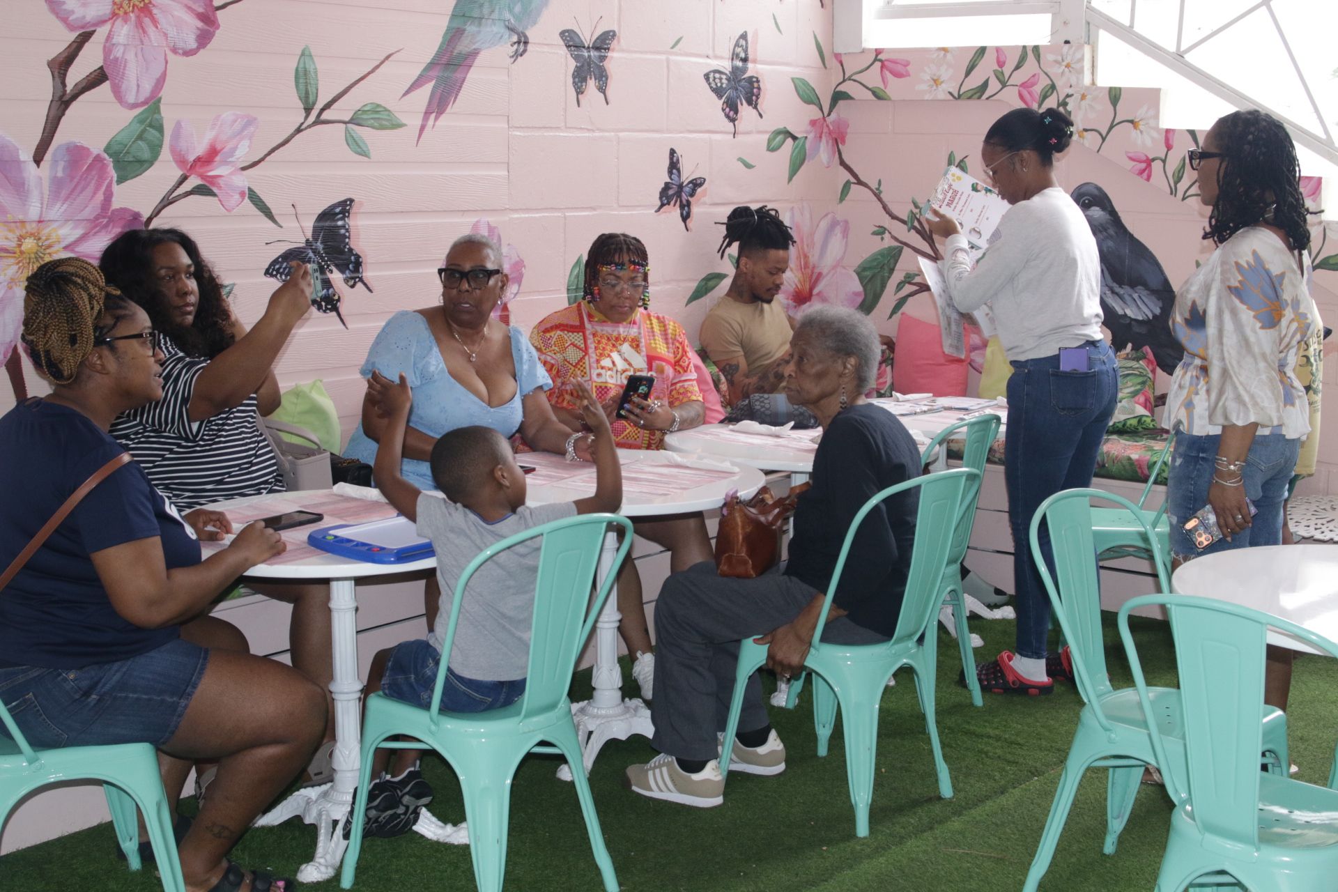Community meeting indoors with people seated around tables, one person standing and speaking