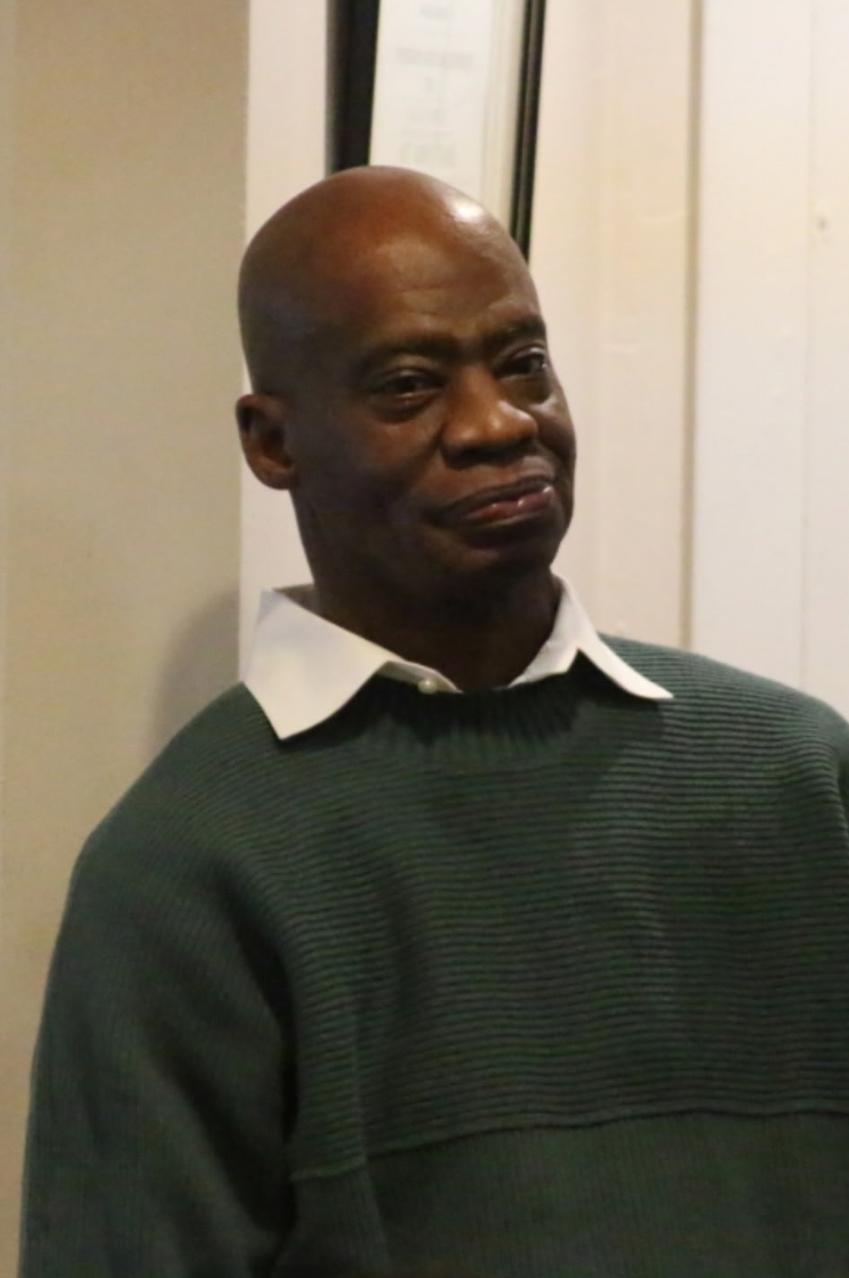 Man in a dark green sweater and white-collared shirt smiling in a doorway