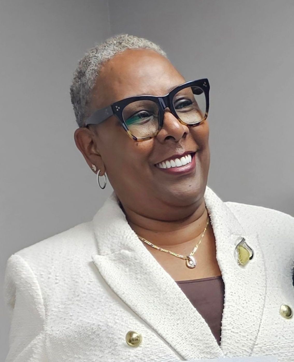 A woman wearing glasses and a white jacket is smiling.