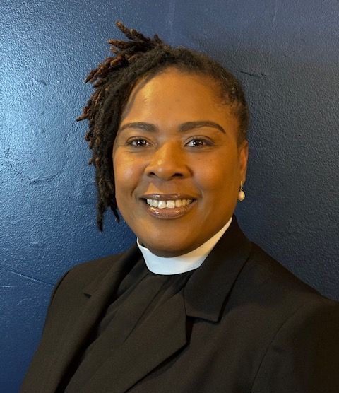 A woman with dreadlocks is wearing a black suit and smiling.