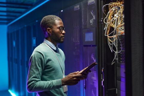 A man is using a tablet in a server room.