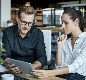 A man and a woman are sitting at a table looking at a tablet.