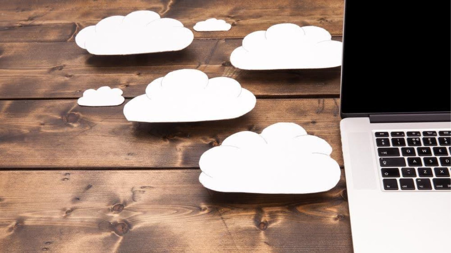 A laptop computer is sitting on a wooden table next to a bunch of paper clouds.