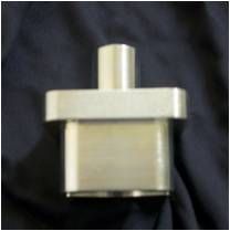 Metal cylindrical connector with a rectangular base, placed on a dark blue surface.