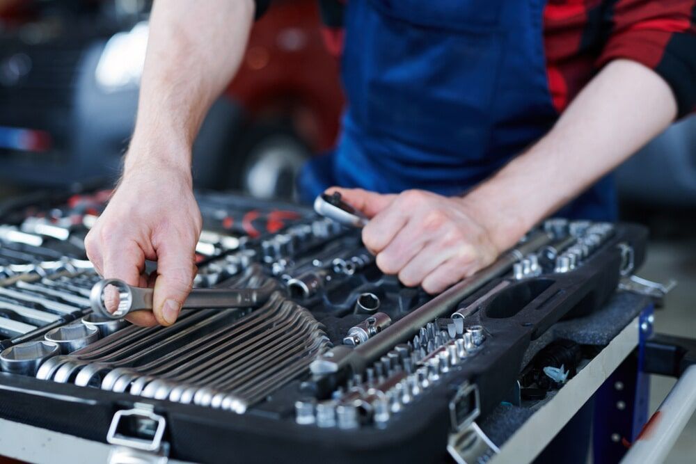 A Man Is Working On A Car In A Garage While Holding A Wrench — Dore's Goodyear Autocare Tully In Tully, QLD