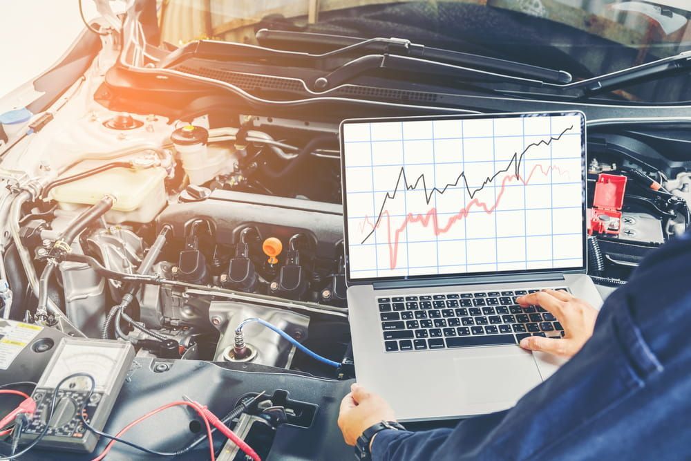A Man Is Using A Laptop Computer While Working On A Car — Dore's Goodyear Autocare Tully In Tully, QLD